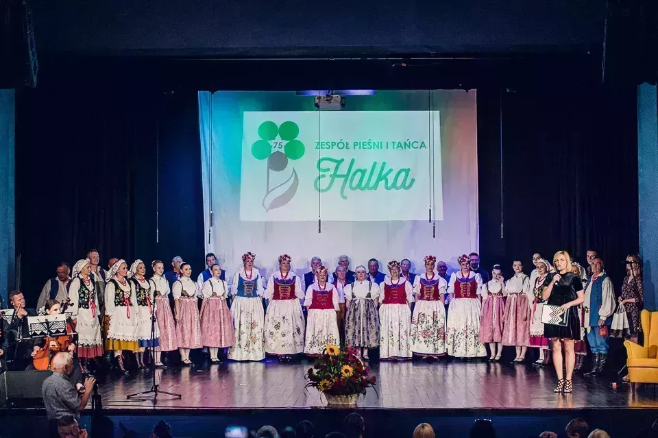 Zespół pieśni i tańca halka ubrany w stroje ludowe, stojący w szeregu na scenie w miejskim domu kultury w lublińcu